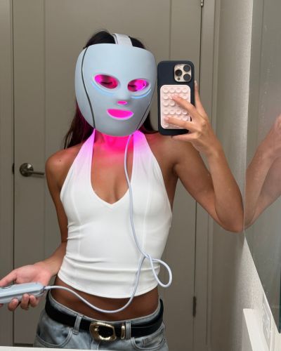 Mujer tomándose una selfie con la Shark CryoGlow puesta y luz rosa encendida; sostiene el control del dispositivo.