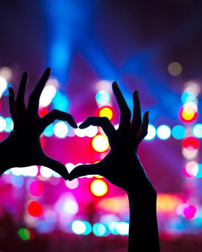 Silueta de manos formando un corazón frente a luces de escenario y público, imagen asociada a la emoción del Corona Capital 2026.
