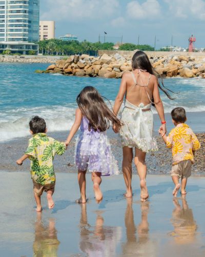 Mamá caminando con tres niños en la orilla del mar, imagen asociada a las vacaciones de verano tras el fin del ciclo escolar oficial.
