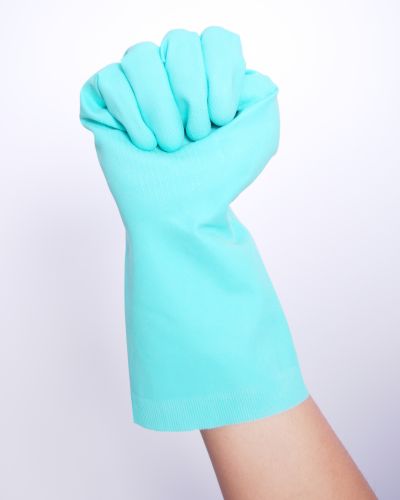 Brazo con guante de limpieza color turquesa levantando el puño sobre fondo blanco, destacando el material tipo guantes de látex.