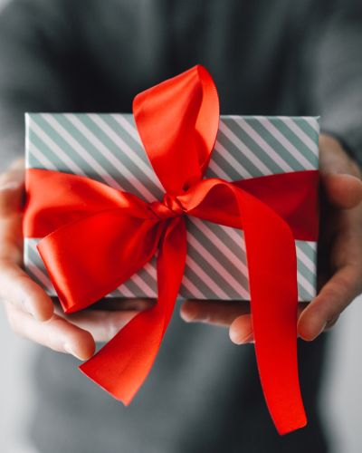 Manos sosteniendo una caja de regalo con papel a rayas y un moño rojo grande, ideal como idea de regalos para mamá.