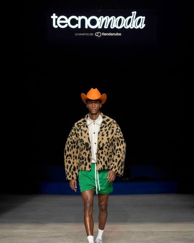 Modelo en pasarela de Tecnomoda México con sombrero vaquero y abrigo animal print, frente al escenario con el logo del evento.