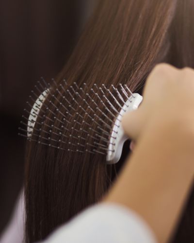 Mano cepillando cabello lacio con un cepillo de cerdas metálicas, como parte de una rutina de peinado.