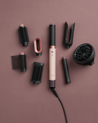 Multiestilizador de Dyson con varios accesorios de peinado acomodados sobre fondo liso, incluyendo cepillos y boquillas.