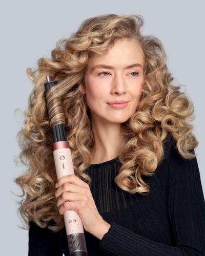 Mujer con cabello rizado usando un rizador tipo barra del multiestilizador de Dyson para definir ondas y rizos.
