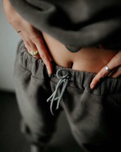 Persona ajustando el resorte del pantalón en la zona del abdomen, un gesto asociado a incomodidad o inflamación abdominal.