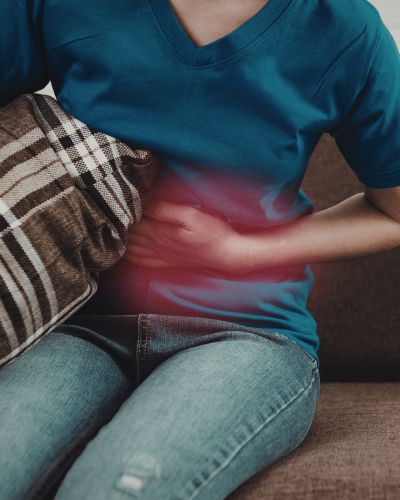 Persona sentada con una mano sobre el abdomen, representando dolor o malestar relacionado con intestino irritable