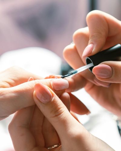 Persona aplicando esmalte de uñas con brocha sobre una uña natural, como parte de una rutina para fortalecer el manicure.