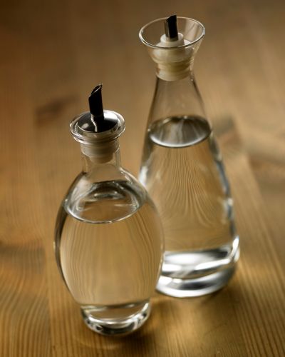 Dos botellas de vinagre sobre una mesa de madera, elemento principal del truco de belleza con vinagre para mejorar el esmalte.