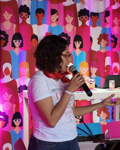 onente hablando con micrófono frente a un fondo ilustrado de personas, durante una charla del Festival Ciclo M 2026 sobre salud menstrual.