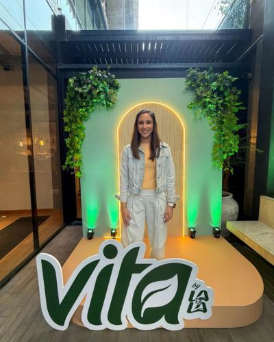 Alejandra Patiño posando en un photo spot con el logo “Vita” y decoración verde, durante un evento de lanzamiento de bebidas vegetales.