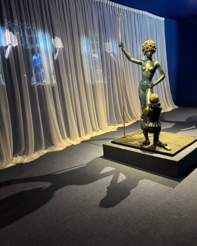 Escultura de una figura fantástica sobre pedestal, iluminada frente a cortinas blancas, dentro de la exposición de Dalí en la CDMX