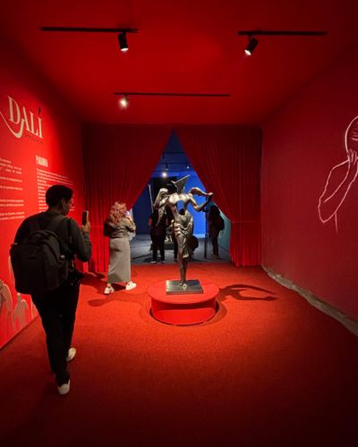 Sala roja de la muestra Dalí: Escenografía de un sueño, con una escultura al centro, visitantes y cortinas que conducen a otra sección de la exposición